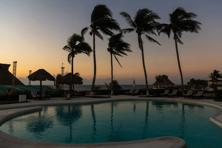 A wide angle view of a pool with Palm Trees in the background during sunrise.
