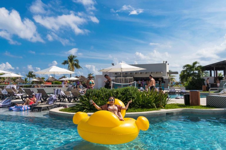 A guest sitting on a giant pool inflatable with their hands up.