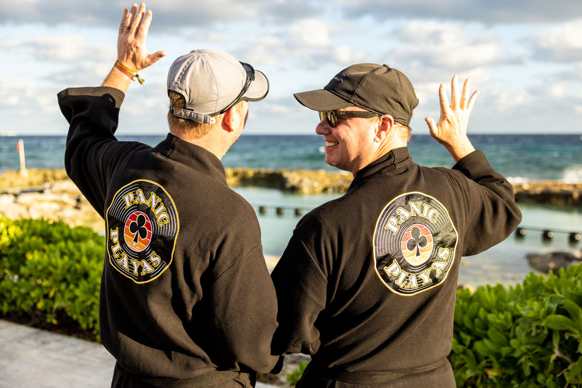 A group photo from behind of guests in their Playas Club black loyalty robes showing off the "Panic Playas" logo.