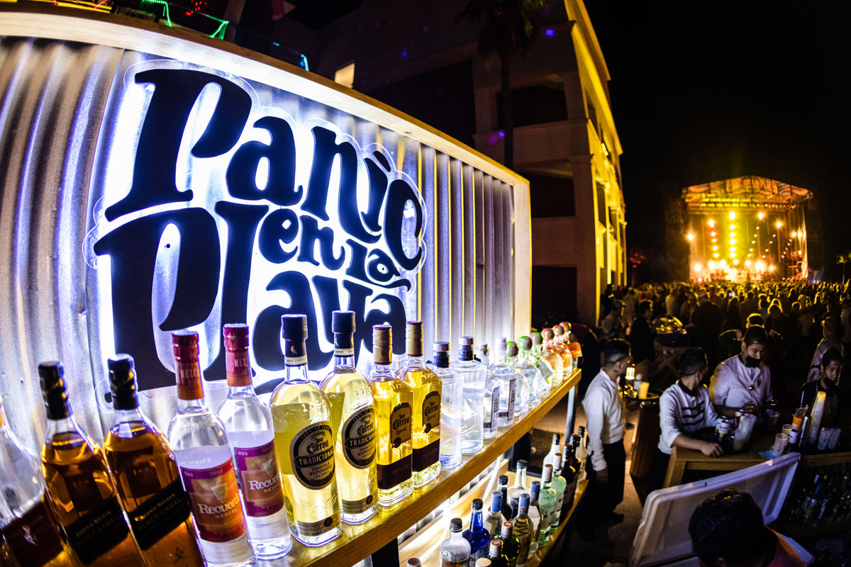 A Panic en la Playa sign behind a wall of drinks at a bar.