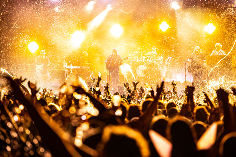 A close up photo of Widespread Panic performing on the Main Stage with bright yellow lights behind them.