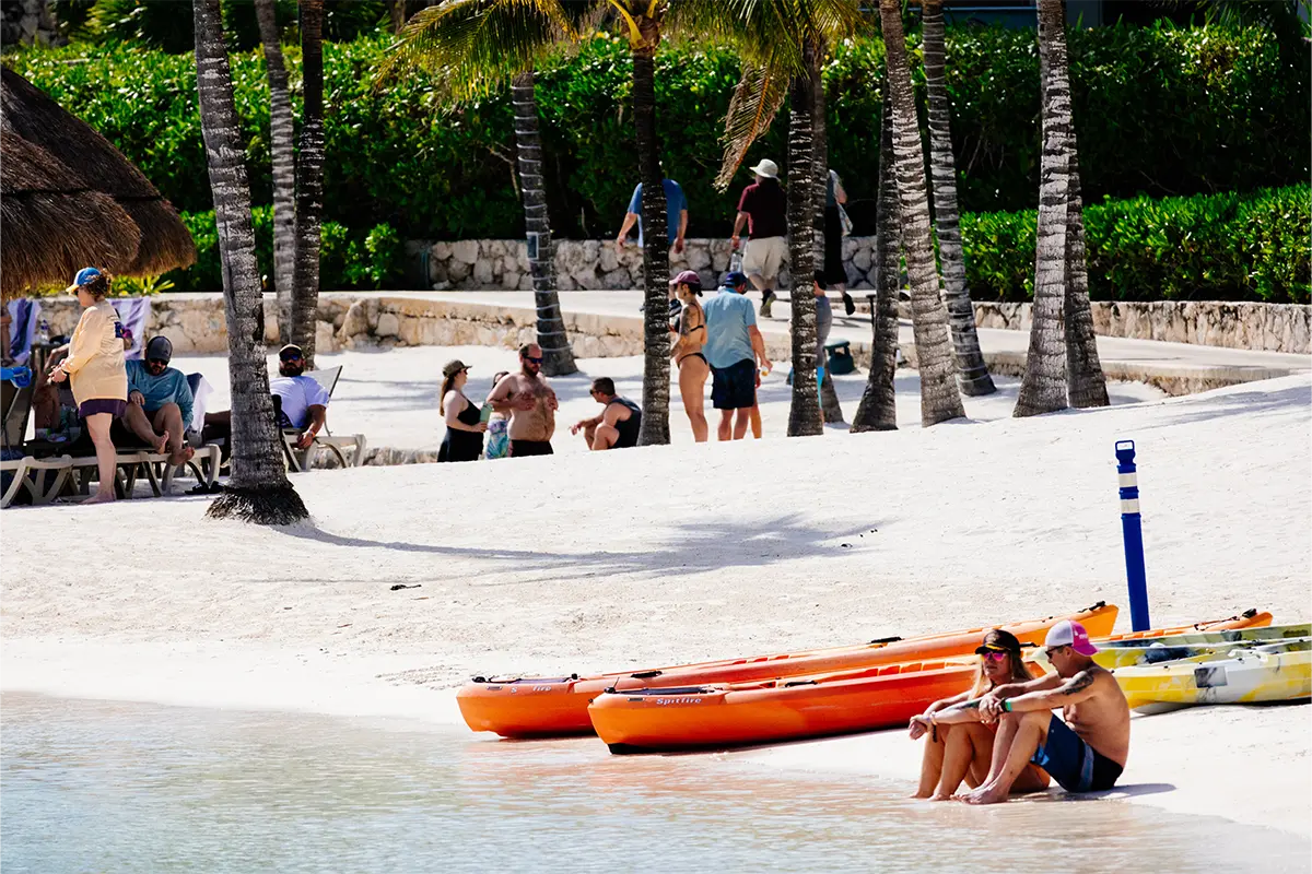 Guests sitting on the beach with kayaks next to them.